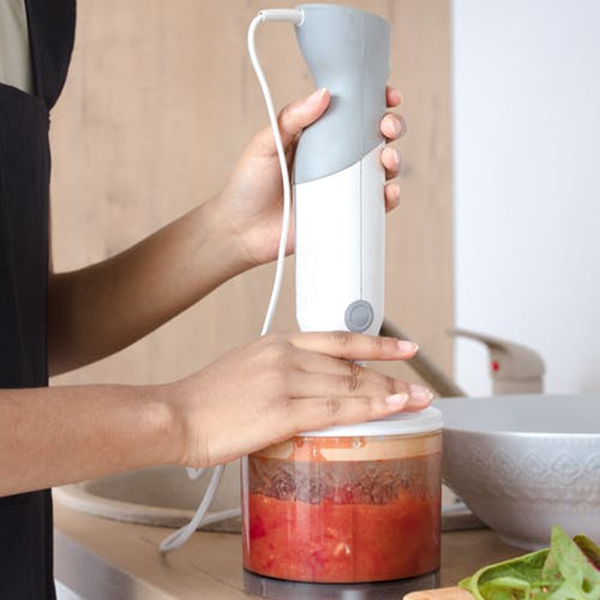 Woman using an immersion blender to meal prep salsa 